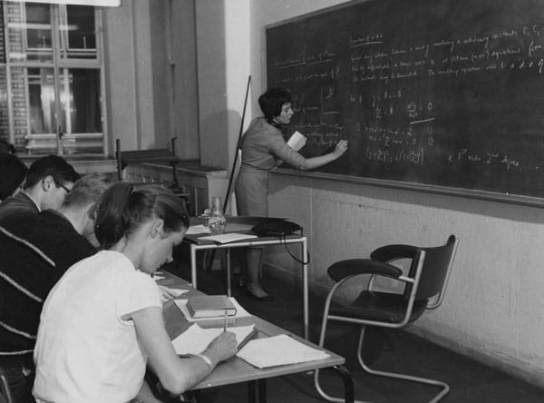 Statistics teacher writing on blackboard in 1960s classroom